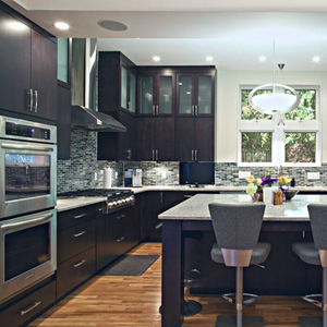 Luxury kitchen with dark brown cabinetry and drawers, gray-and-black mosaic tile backsplash and light-color countertops with marbled dark colors around the appliances and sink and on the large kitchen island